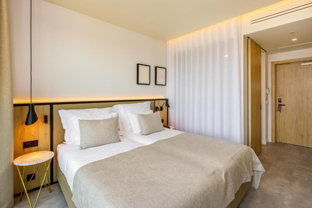 Ein modernes Hotelzimmer mit einem großen Bett, Nachttischen, einer Wandlampe und einer Tür.
