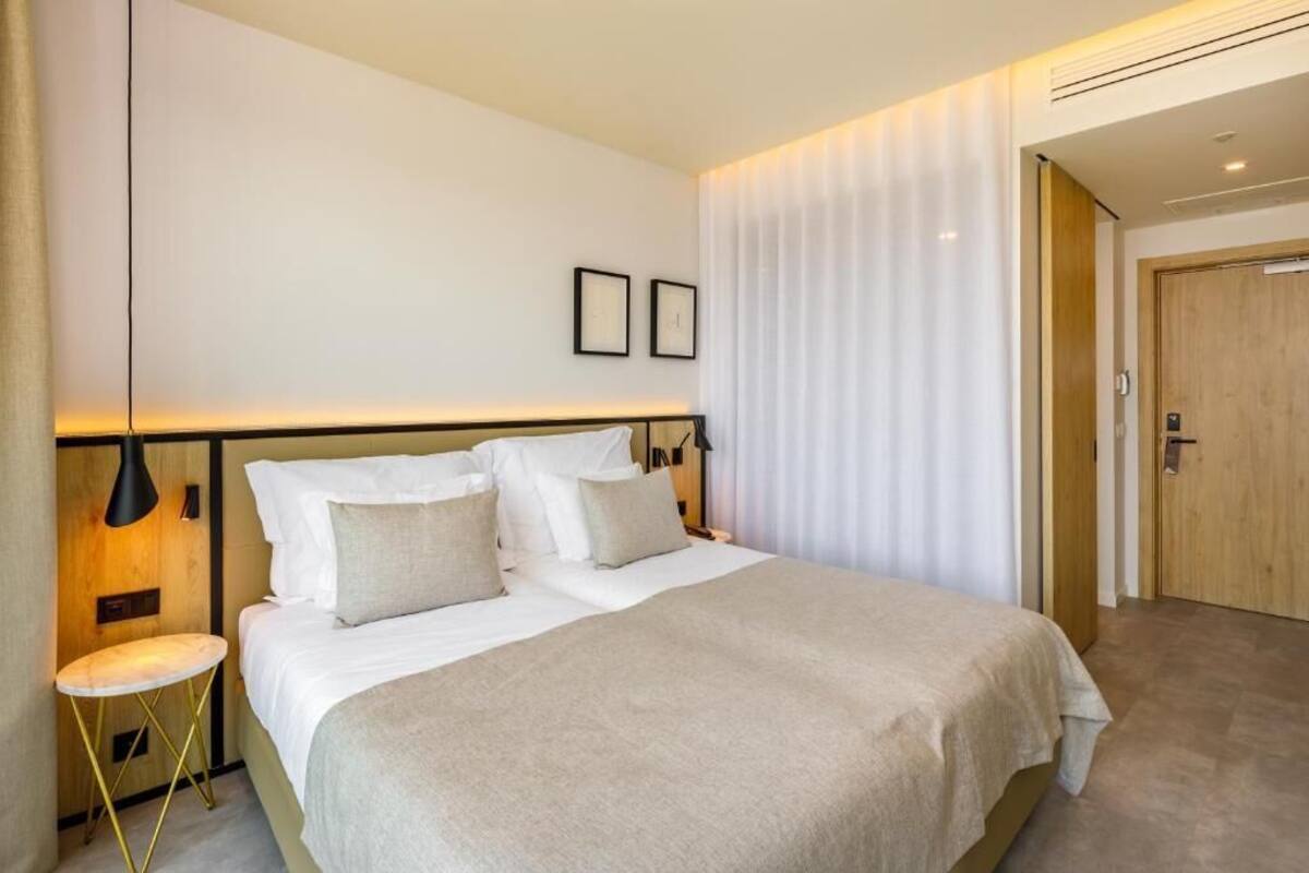 Una habitación de hotel moderna con una cama grande, mesitas de noche, una lámpara de pared y una puerta.