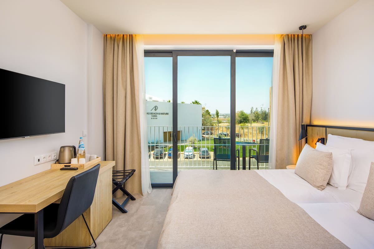 Habitación de hotel con cama, escritorio, silla, televisor y balcón con vistas al exterior.