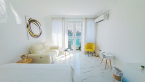 Ein Hotelzimmer mit Bett, Sofa, gelbem Sessel, Schreibtisch und Meerblick durch das Fenster.