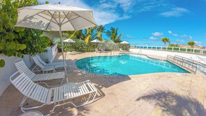 Zona de piscina con sillones blancos, una sombrilla grande y vista al océano.