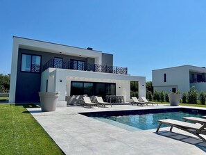 Una casa moderna de dos pisos con piscina, mobiliario exterior y césped cuidado.