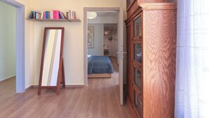A room with a wooden floor, a bed with a blue bedspread, a wooden cabinet, and a bookshelf with various books.
