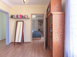Una habitación con piso de madera, una cama con colcha azul, un armario de madera y una estantería con varios libros.