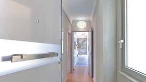 A modern hallway with a wooden floor, a white wall with a built-in shelf, and a door leading to a bathroom with a bathtub and a window.