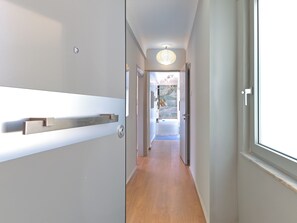 A modern hallway with a wooden floor, a white wall with a built-in shelf, and a door leading to a bathroom with a bathtub and a window.