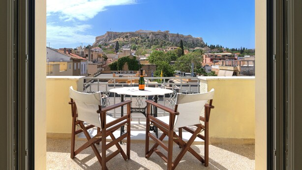 A balcony with a table and chairs, overlooking a cityscape with a prominent hill and buildings.