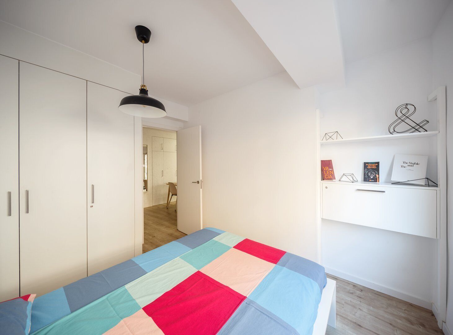 Un dormitorio con cama, armario, escritorio y estante con libros y objetos decorativos.