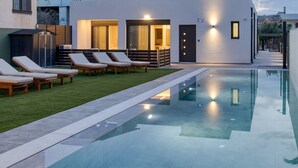 A modern outdoor pool area with lounge chairs and a well-lit entrance. - Potame Suite by Estia Pool View (Hersonissos)