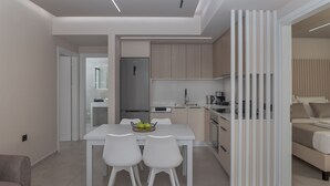 A modern kitchen with white cabinetry, a dining area with a white table and chairs, and a bedroom with a bed and a nightstand. - Potame Suite by Estia Pool View (Hersonissos)