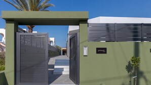 A gated entrance with a palm tree, a sign reading "POURNE," and a staircase leading to a building.
