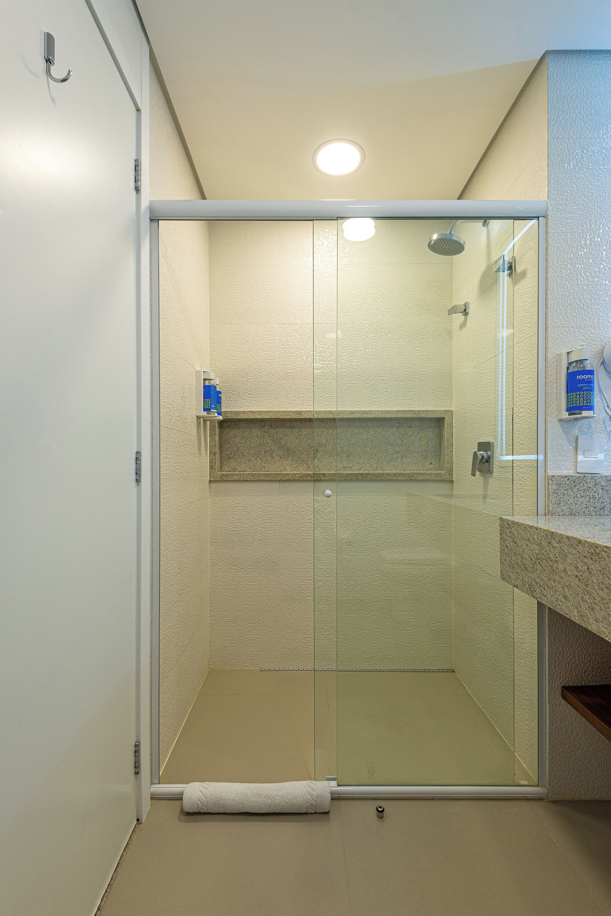 A modern shower with a glass door, a built-in shelf, and a towel on the floor.