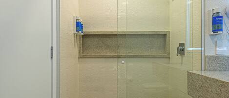 A modern shower with a glass door, a built-in shelf, and a towel on the floor.