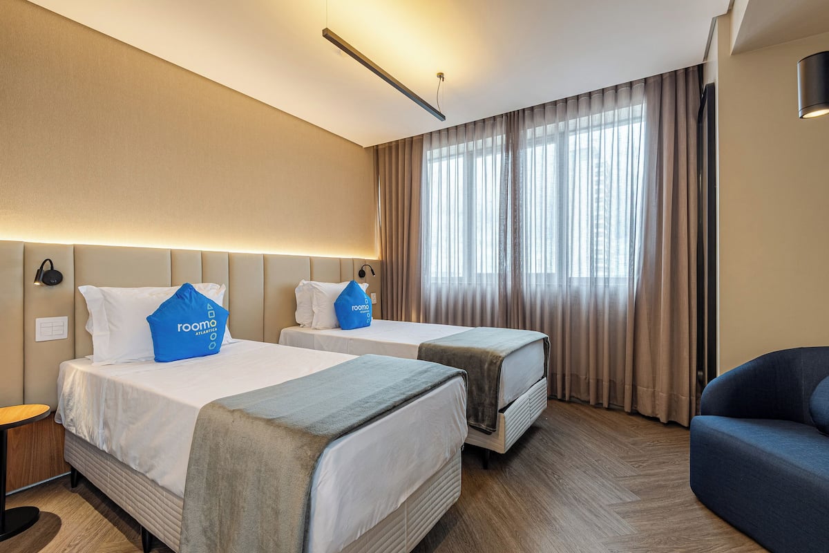 A hotel room with two beds, a sofa, a desk, and a large window with curtains.