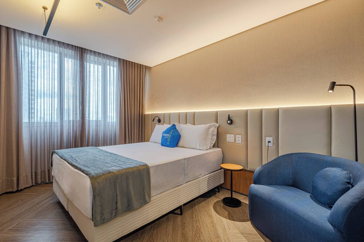A hotel room with a large bed, a blue armchair, and a bedside table.