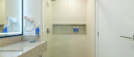A modern bathroom with a granite countertop, a mirror, a hairdryer, and a shower area.