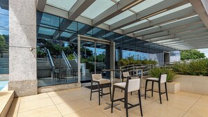 An outdoor seating area with modern chairs and a glass enclosure, overlooking a staircase and greenery. - Roomo Transamerica Goiânia Orion (Goiânia)
