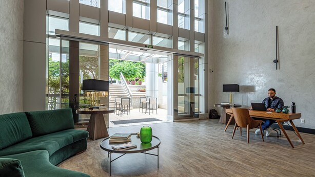 A spacious lobby with a green sofa, a round coffee table, and a desk with a laptop. - Roomo Transamerica Goiânia Orion (Goiânia)