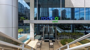 A modern building with a glass facade, outdoor seating area, and a visible pool. - Roomo Transamerica Goiânia Orion (Goiânia)