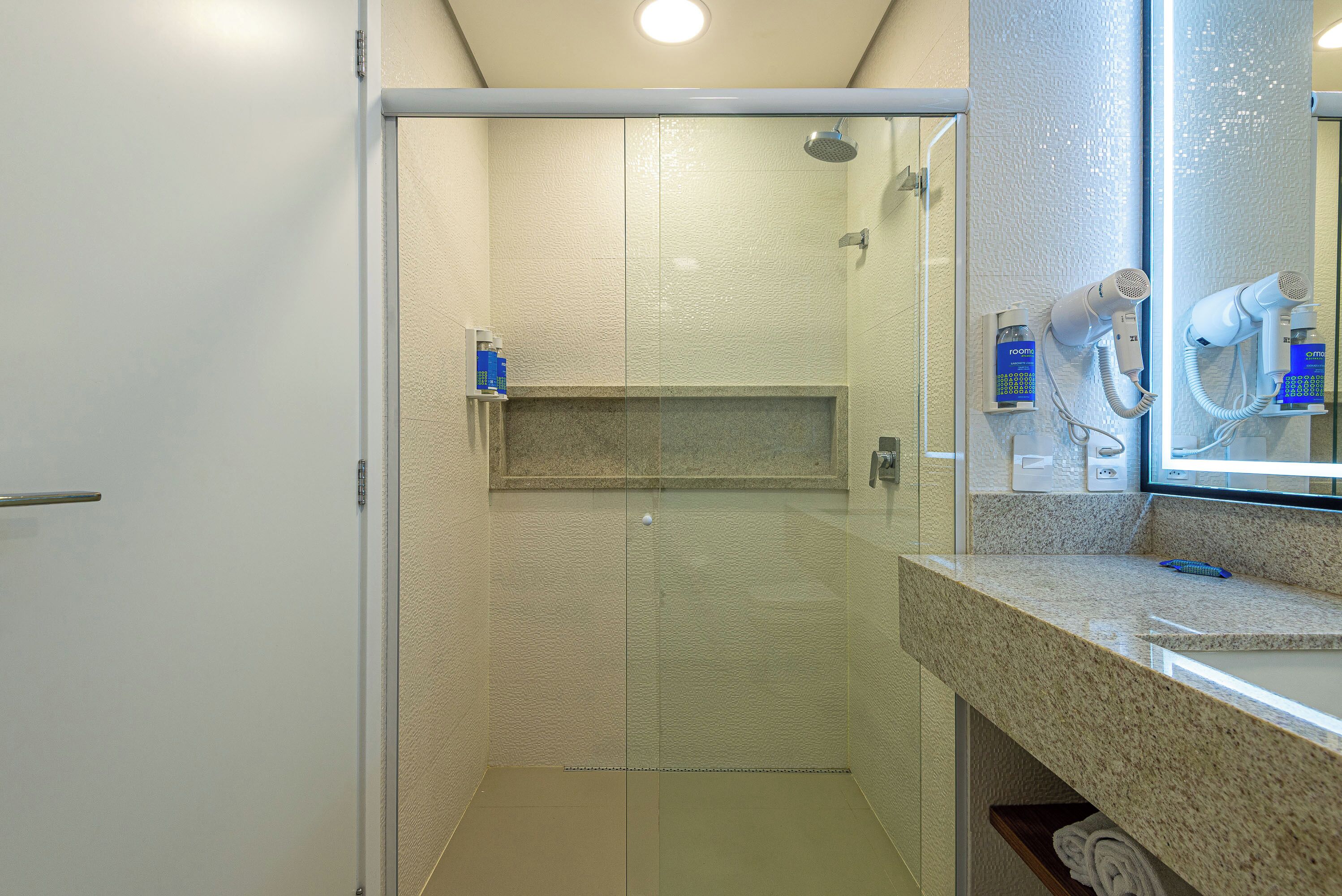 A modern bathroom with a glass shower enclosure, a vanity with a mirror, and a hairdryer on the counter.