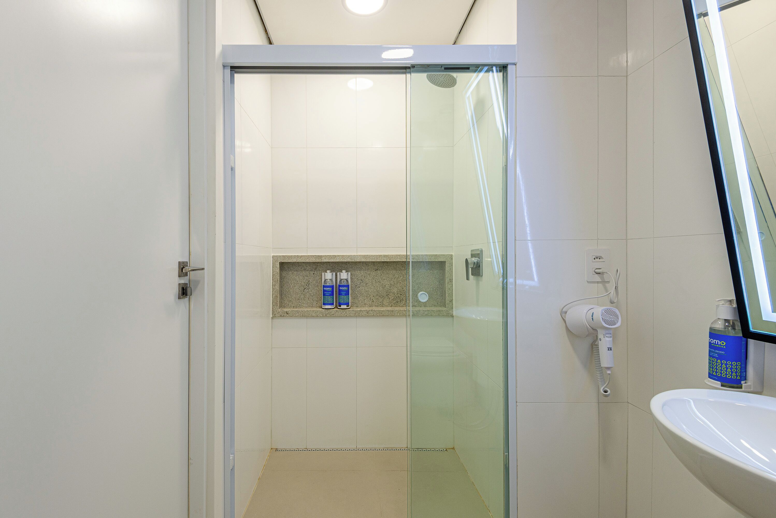 Un bagno moderno con doccia vetro, lavandino e ripiano con articoli da toilette.