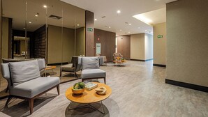 A modern waiting area with sofas, a coffee table, and a small table with a plant. - Roomo Transamerica Goiânia Orion (Goiânia)