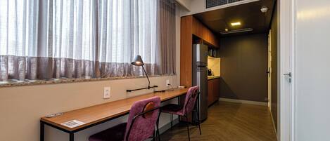 A compact kitchen with a refrigerator, a wooden countertop, and a window with sheer curtains.