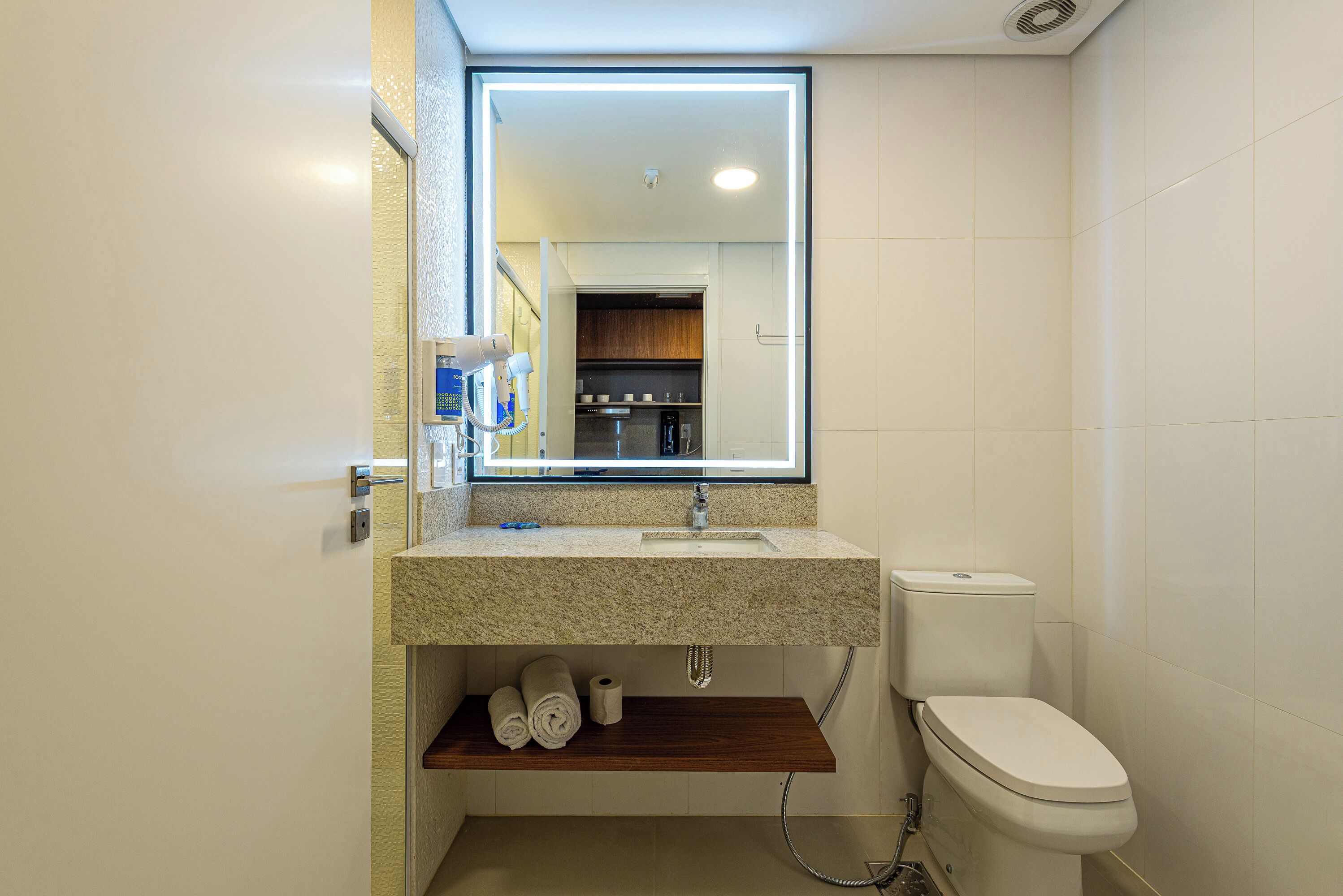 Une salle de bain avec un comptoir en granit, des toilettes, un miroir et une douche.