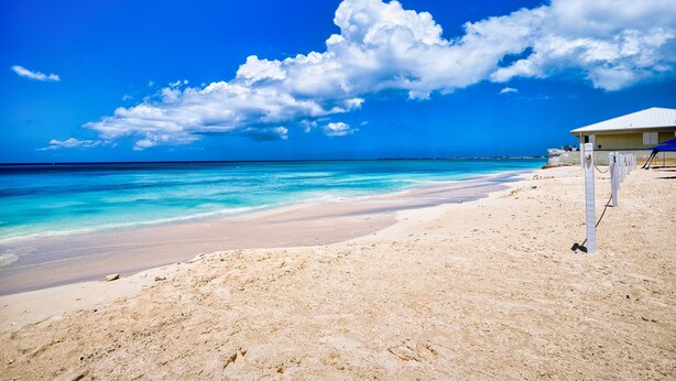 A beach with clear turquoise waters, a sandy shore, and a building with a white roof.