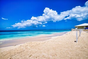 Ein Strand mit klarem türkisblauem Wasser, einem sandigen Ufer und einem Gebäude mit weißem Dach.