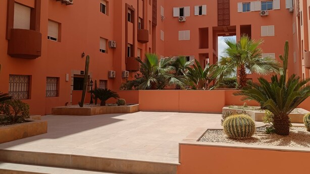 Un edificio de varios pisos con balcones, unidades de aire acondicionado y un patio con escalones y cactus.