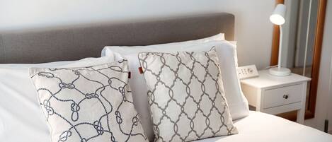 A neatly made bed with two patterned pillows and a bedside table with a lamp and a power outlet.