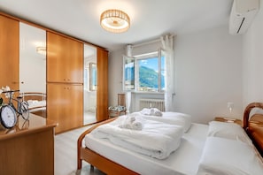 Hotelkamer met een bed, een houten garderobe, een spiegel, een fiets en uitzicht op bergen.