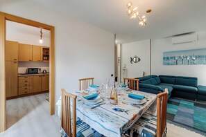 Un coin repas avec une table dressée pour quatre personnes, une cuisine avec des meubles en bois et un salon avec un canapé bleu.