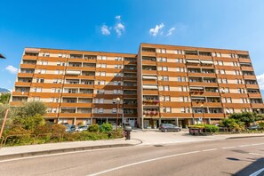 A multi-story residential building with balconies, a parking area, and a street view.