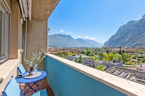 Un balcón con mesa y sillas, con vista a un paisaje urbano y montañas al fondo.