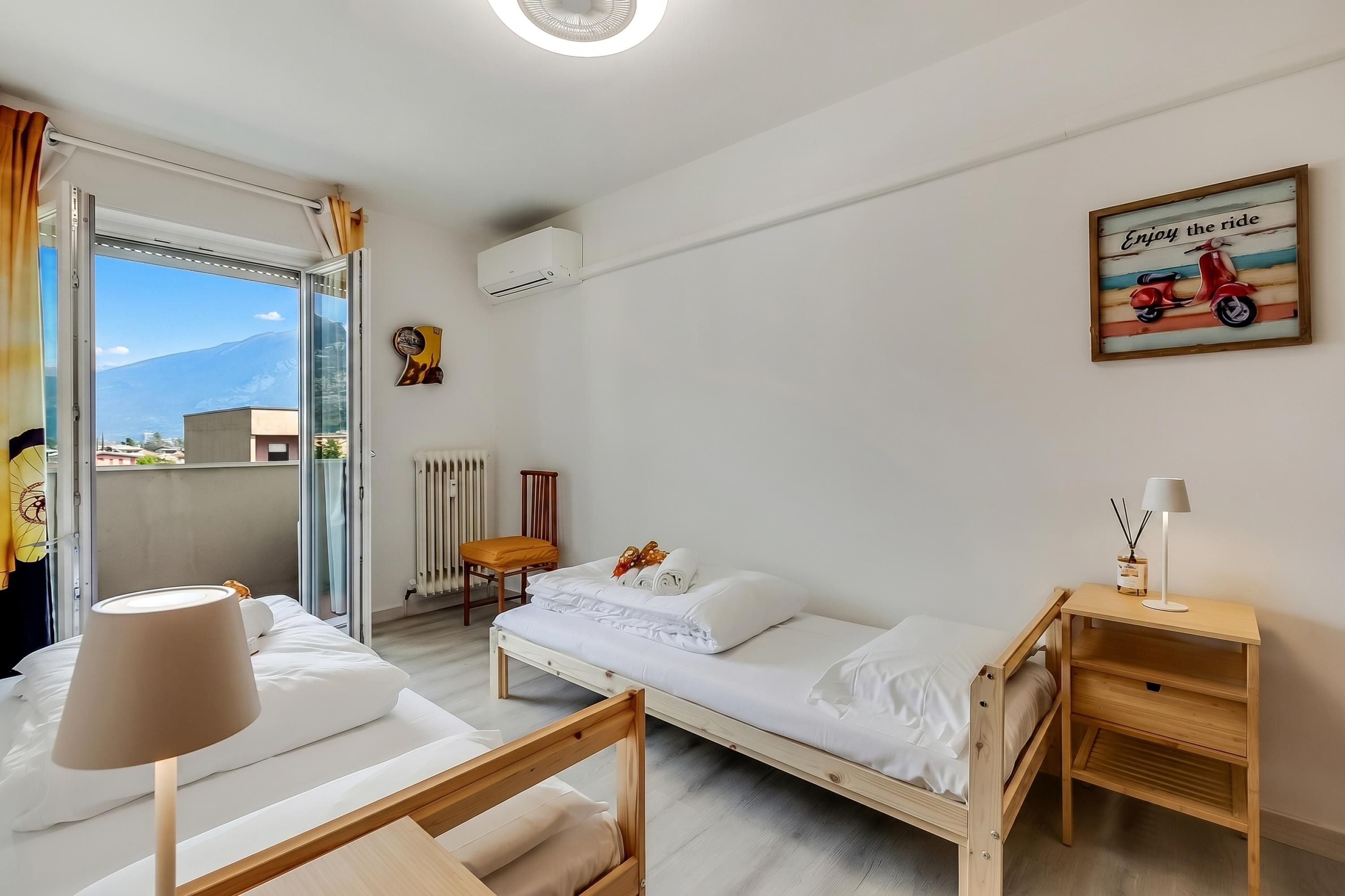 Ein Einzelbett mit Holzrahmen, ein Nachttisch mit Lampe, eine Heizung und ein Fenster mit Vorhängen.