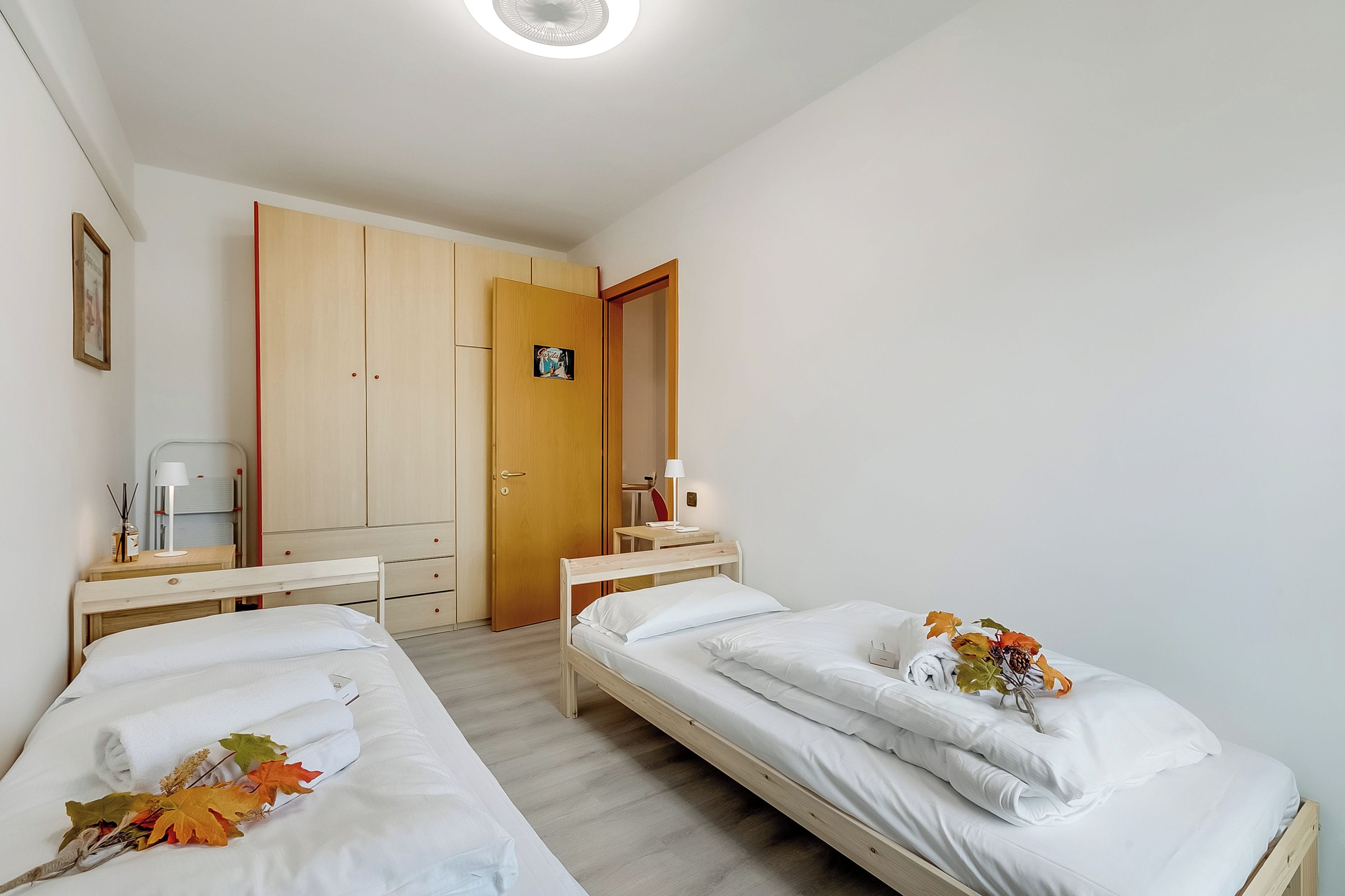 Une chambre propre et bien éclairée, avec deux lits simples, une armoire en bois, un bureau et une chaise.