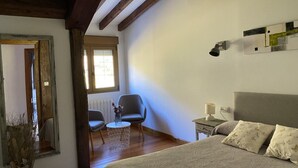 A bedroom with a large bed, a chair, a small table, and a window with blinds. - Viviendas Rurales Valverde (Cabezon de Liebana)