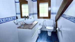 A bathroom with a sink, mirror, toilet, bidet, and a wooden-framed window. - Viviendas Rurales Valverde (Cabezon de Liebana)