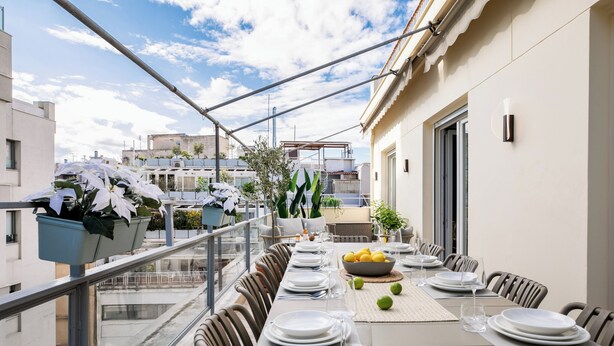 Un área de comedor en la azotea con una mesa larga dispuesta para una comida, rodeada de sillas, y vistas panorámicas de la ciudad.