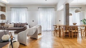 Una sala de estar moderna con un sofá, sillas, una mesa de comedor y un ventanal con cortinas translúcidas.