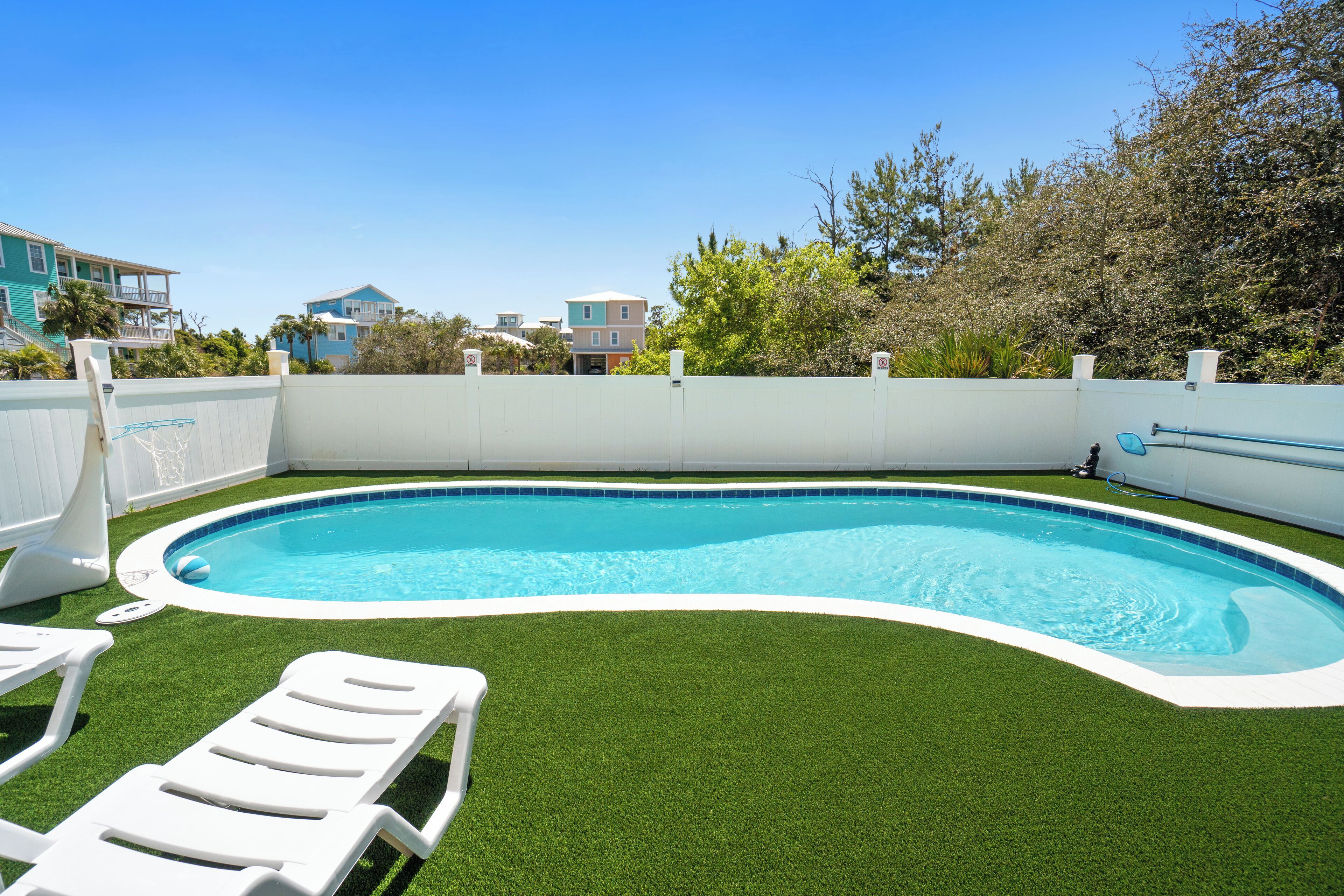 A swimming pool with artificial grass, a white fence, and a clear blue sky.
