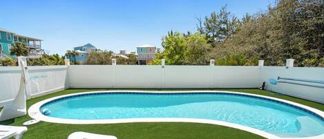 A swimming pool with artificial grass, a white fence, and a clear blue sky.