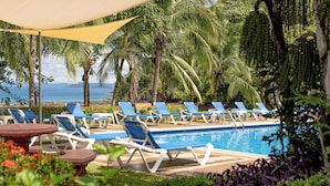 A poolside area with lounge chairs and a pool, surrounded by palm trees and a view of the ocean.