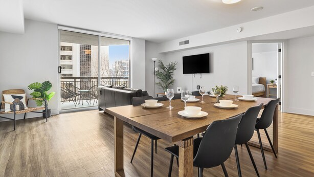 Un comedor moderno con una mesa de madera para cuatro personas, un sofá y un televisor montado en la pared.