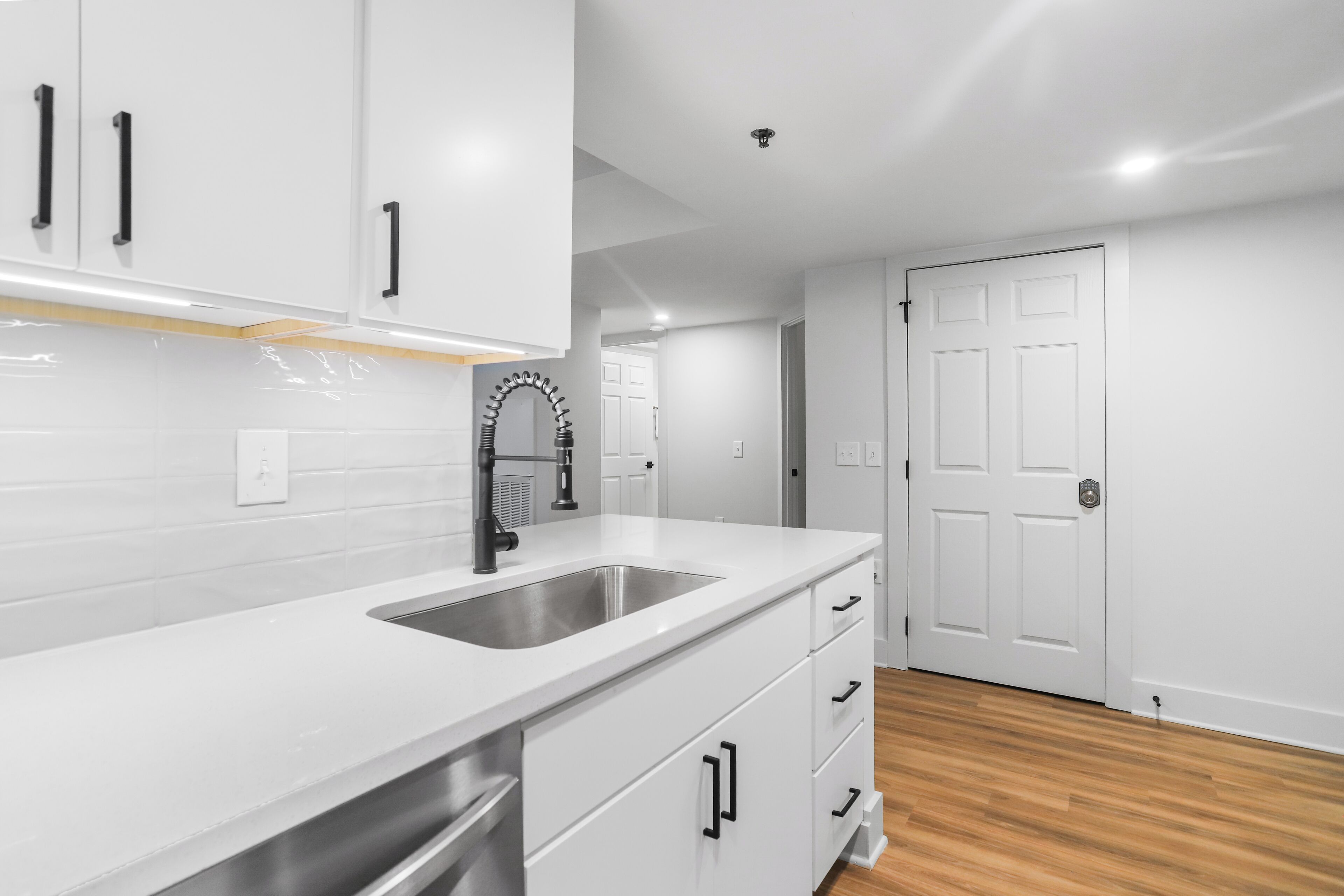 A modern kitchen with white cabinets, a stainless steel sink, and wooden flooring.