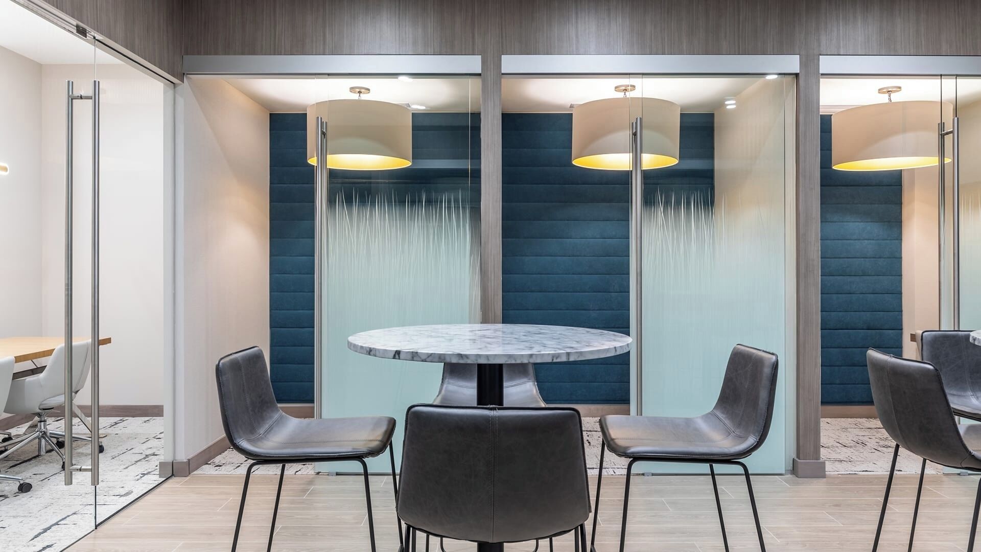 Una sala de reuniones moderna con una mesa redonda, cuatro sillas y un panel de vidrio con fuente de agua.