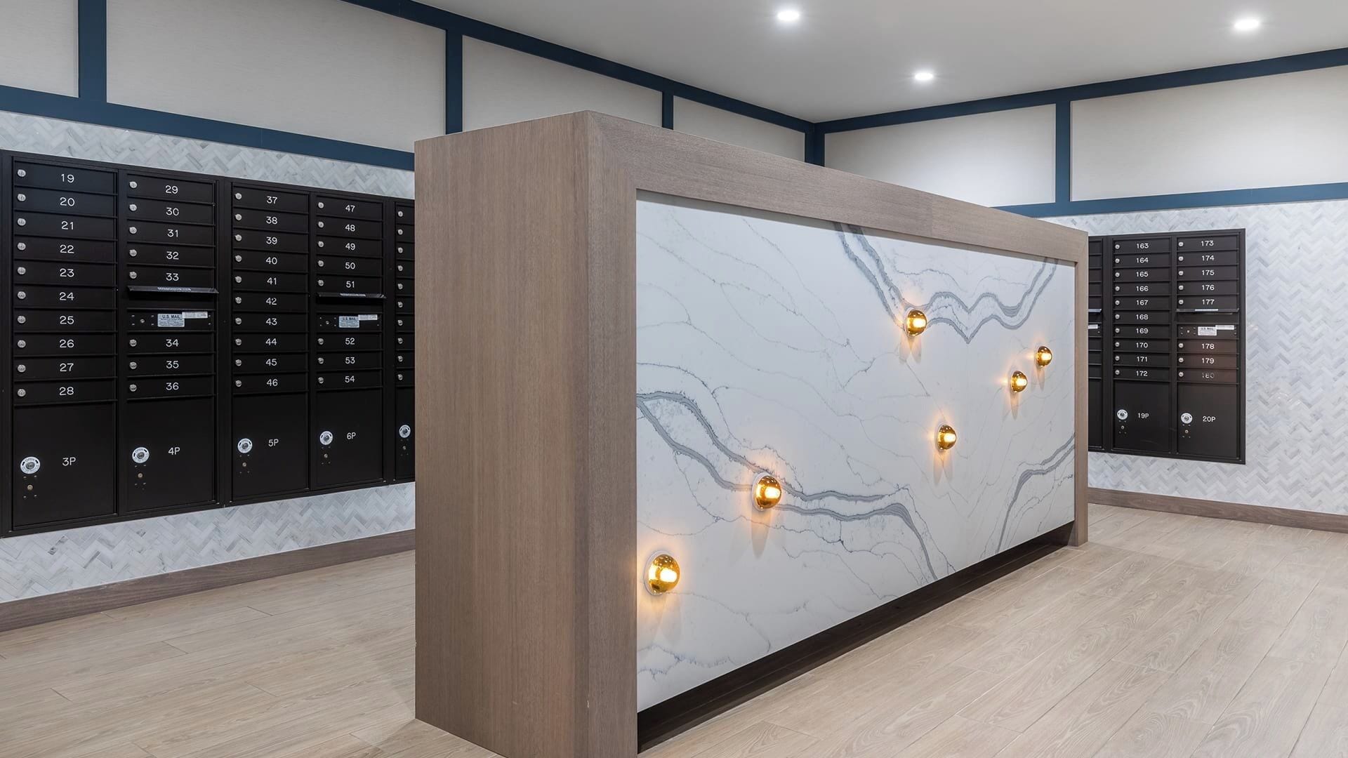 A modern reception desk with a marble top and wooden frame, flanked by black mailboxes with labels.