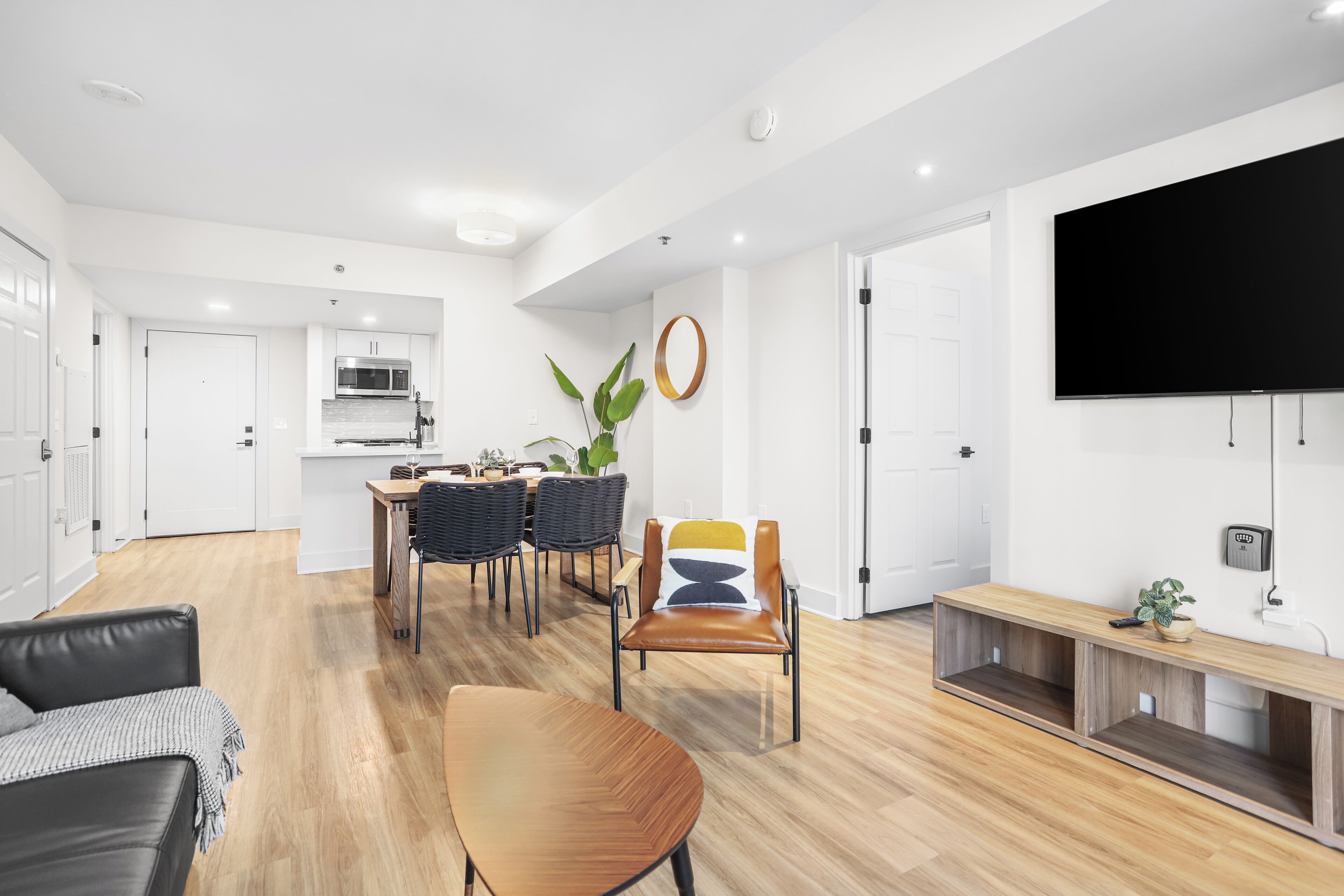 Ein modernes Wohnzimmer mit Esstisch aus Holz, einer Ledersofa und einem an der Wand befestigten Fernseher.
